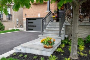 New stone front steps with black railings, a flower planter and a fresh asphalt driveway